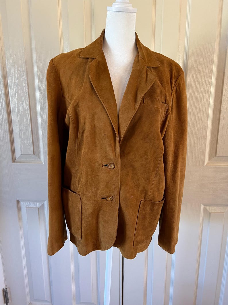 May include: A brown suede blazer with a notched collar, two button closure, and two flap pockets.