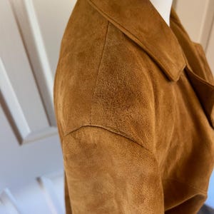 May include: A close-up of the brown suede shoulder of a jacket. The suede is soft and textured.