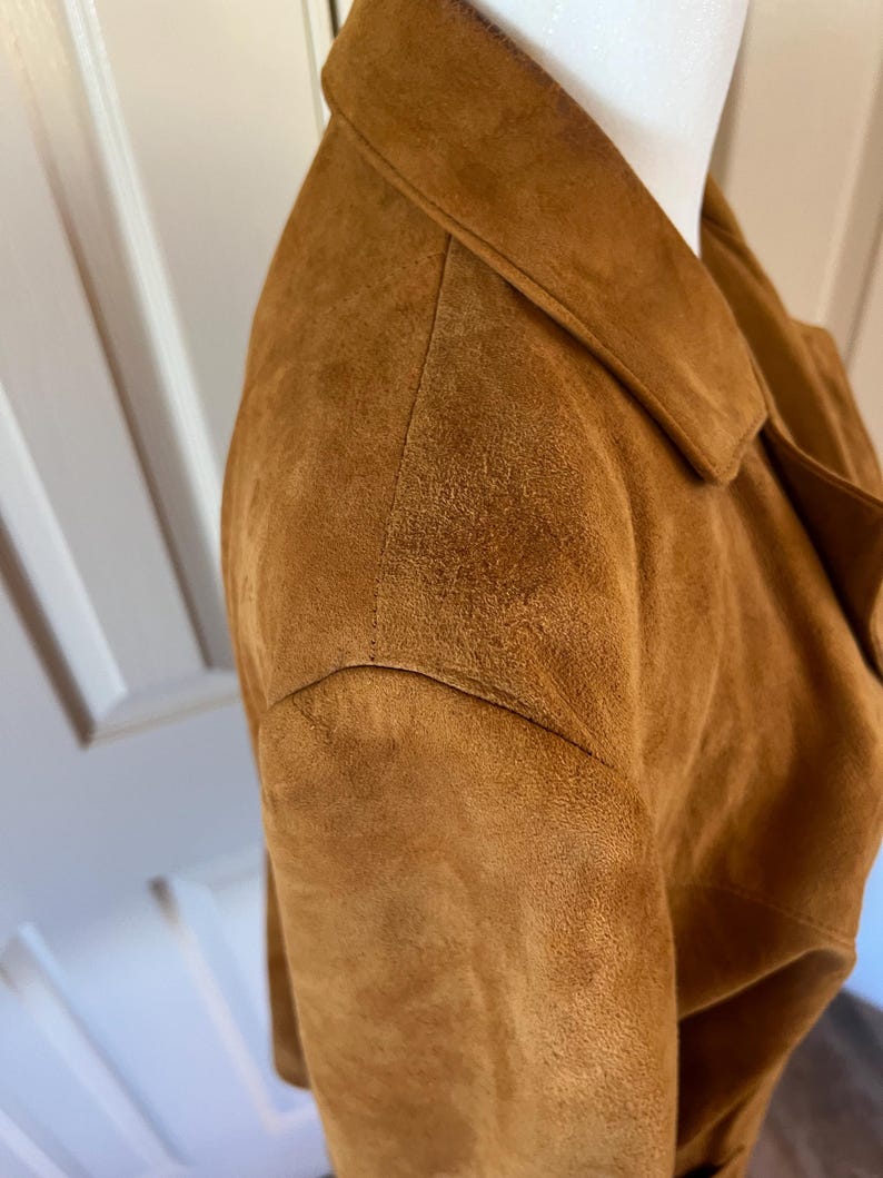 May include: A close-up of the brown suede shoulder of a jacket. The suede is soft and textured.