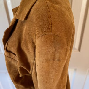 May include: A brown suede jacket with a collar and long sleeves. The jacket is made of a soft, textured material.