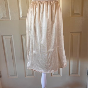 May include: A beige satin slip skirt with a lace trim. The skirt is on a white mannequin.