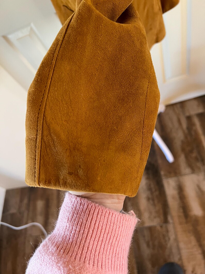 May include: Close-up of the brown suede fabric of a jacket sleeve.