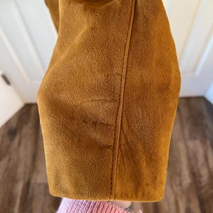 May include: Close-up of the brown suede fabric of a jacket. The fabric has a soft, fuzzy texture.
