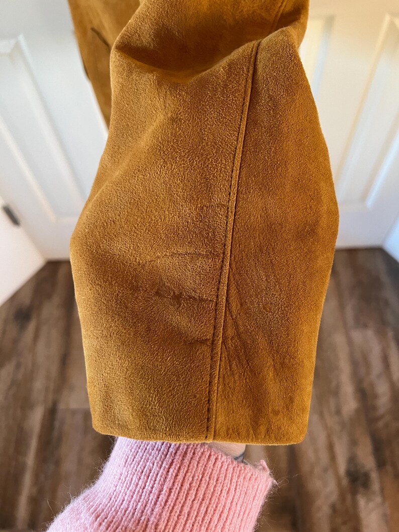 May include: Close-up of the brown suede fabric of a jacket. The fabric has a soft, fuzzy texture.