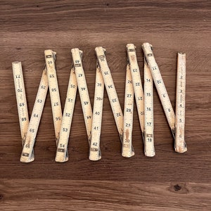 May include: A set of ten vintage wooden folding rulers, each with a different number of inches marked on them. The rulers are laid out in a row on a wooden surface.