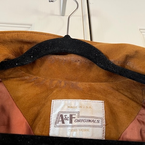 May include: A brown suede jacket with a brown satin lining. The jacket has a label that reads "Made in U.S.A. A&F Originals New York".