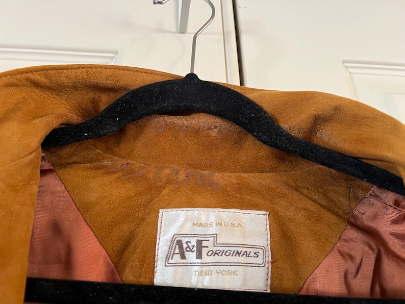 May include: A brown suede jacket with a brown satin lining. The jacket has a label that reads "Made in U.S.A. A&F Originals New York".