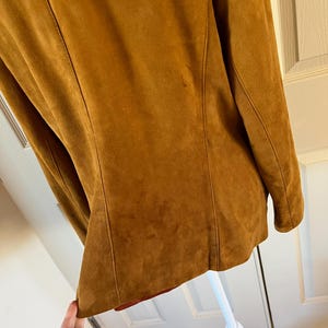 May include: A brown suede jacket with a long sleeve and a collar. The jacket is on a white mannequin.