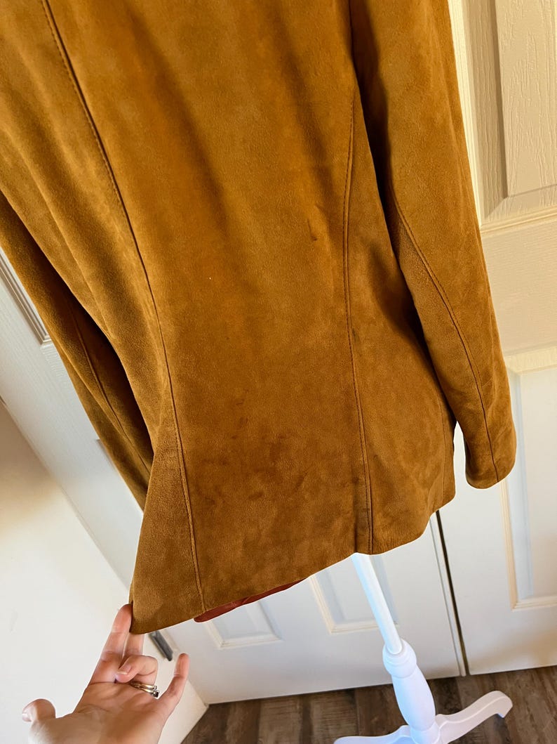 May include: A brown suede jacket with a long sleeve and a collar. The jacket is on a white mannequin.