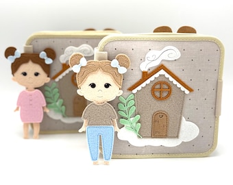 May include: Felt doll with brown hair and blue bows, wearing a pink dress. A felt house with a brown roof and white accents is featured on a beige background. The doll is standing next to a felt house with a cloud and green leaves.