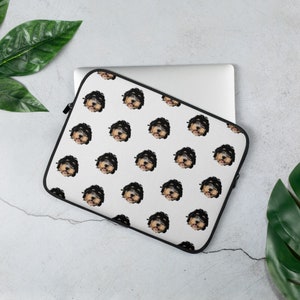 May include: White laptop sleeve with a repeating pattern of a black and brown dog's face. The dog is looking directly at the camera with its tongue sticking out.