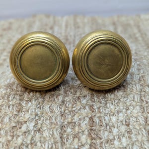 May include: Two antique brass door knobs with a circular design and a raised rim.