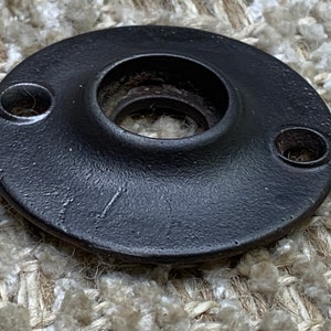 May include: Black metal door knob backplate with two screw holes. The backplate has a raised lip around the center hole.