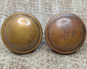 May include: Two antique brass door knobs with a rounded top and a slightly raised edge. The knobs have a worn, aged patina.