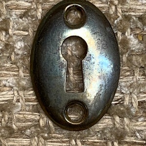 Op de afbeelding: Een zilveren ovale sleutelgatbedekking met twee kleine gaten aan beide zijden.