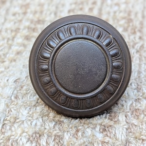 May include: A dark brown metal knob with a decorative, raised, circular design around the edge.