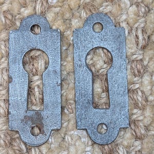 Könnte beinhalten: Zwei antike silberne Schlüssellöcher mit strukturierter Oberfläche.