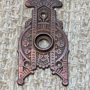 May include: A vintage, ornate, copper-colored door knocker with intricate geometric designs and a circular opening for the knocker.