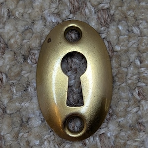 May include: A gold-colored oval keyhole cover with two small holes on either side.