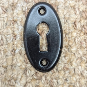 Könnte beinhalten: Schwarzer ovaler Schlüsselschlitzabdeckung mit zwei kleinen Löchern an jeder Seite.