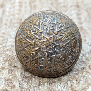 May include: A vintage brass door knob with an intricate floral design. The knob is round and has a raised pattern of flowers and leaves.