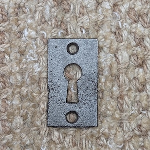 Könnte beinhalten: Ein silberner Schlüsselschlitzabdeckung mit zwei runden Löchern auf beiden Seiten des Schlüsselloches.