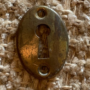 May include: A brass keyhole cover with an oval shape and two small holes on either side. The keyhole is in the centre of the cover.