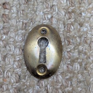 Peut inclure: Un cache-trou de serrure en laiton avec deux petits trous de chaque côté du trou de la serrure. Le cache est de forme ovale et a un aspect usé et vieilli.