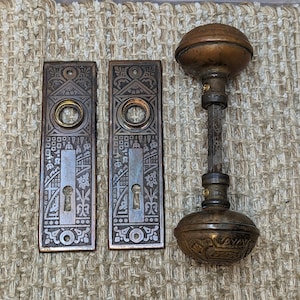 May include: A set of antique door hardware with a decorative design. The set includes two door plates and a knob with a keyhole. The hardware is made of metal and has a silver finish.