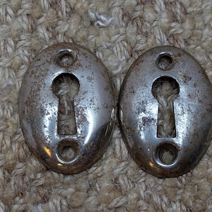 Op de afbeelding: Twee antieke zilveren sleutelgatbeslag met een versleten, verweerde afwerking.