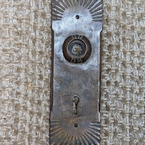 Pode incluir: Placa de porta de latão antigo com uma fechadura, um botão redondo e um design decorativo de sol.