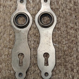 May include: Two antique silver door handles with keyholes. The handles are ornate and have a decorative design.