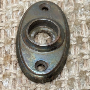 May include: Oval-shaped brass door knob escutcheon with a circular hole in the center and two smaller holes on the sides. The escutcheon has a worn, aged patina.