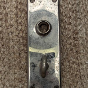 May include: A silver metal door plate with a round hole and a hook. The plate has two small holes on the top and bottom.