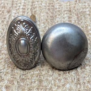 May include: Two silver door knobs, one with an ornate design and the other smooth and round.