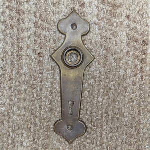 May include: A brass door knob with a keyhole and a decorative design. The knob is a vintage style and has a worn finish.