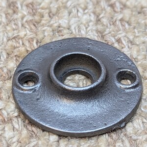 May include: A round, black metal flange with a hole in the centre. The flange has two smaller holes on the sides.