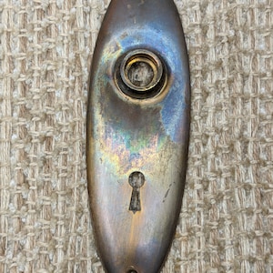 Peut inclure: Une plaque de porte ovale en laiton avec un trou de serrure et un trou de bouton rond. La plaque a une patine usée et vieillie.