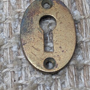 Op de afbeelding: Ovale messingen sleutelgatbedekking met twee kleine gaten aan beide zijden. Het sleutelgat bevindt zich in het midden van de bedekking.