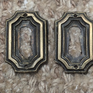 Könnte beinhalten: Zwei antike Schlüsselschilder mit Messing-Finish und einem dekorativen, geometrischen Design.