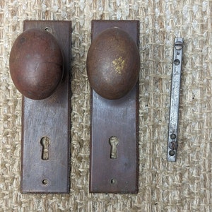 May include: Two antique door knobs with keyholes and round, brown, metal handles. A metal door latch is also pictured.