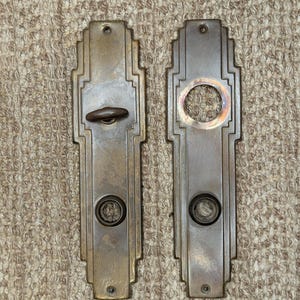 May include: Two antique brass door plates with Art Deco design. Each plate has a keyhole and a decorative circle.