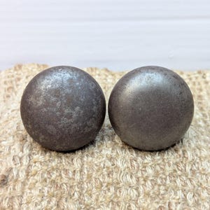 May include: Two round, dark gray metal cabinet knobs with a distressed finish.