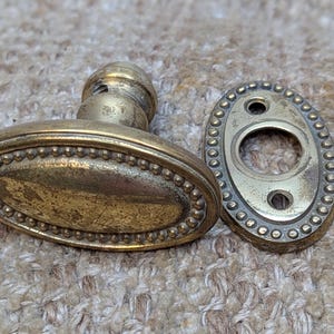 May include: A vintage brass door knob with a beaded edge and an oval-shaped plate. The knob has a decorative design and is in good condition.