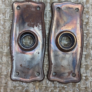 May include: Two antique door knobs with a worn copper finish. The knobs have a round opening in the center and two small holes on the top.