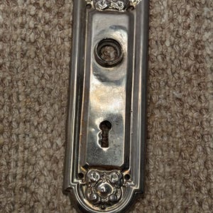 May include: A silver door plate with a keyhole and decorative floral accents.