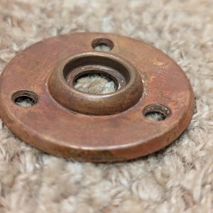 Peut inclure: Une plaque de fond ronde en laiton pour bouton de porte avec trois trous de vis et une grande ouverture circulaire au centre.