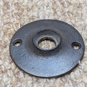 May include: A black metal round plate with a hole in the center. The plate has two small holes on the sides.