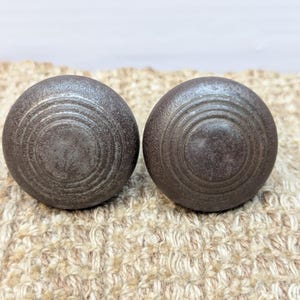 May include: Two dark gray metal drawer knobs with a circular design and concentric grooves.