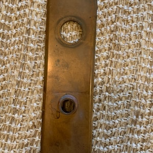 May include: A rectangular brass door plate with two round holes. The plate has a worn, aged look.